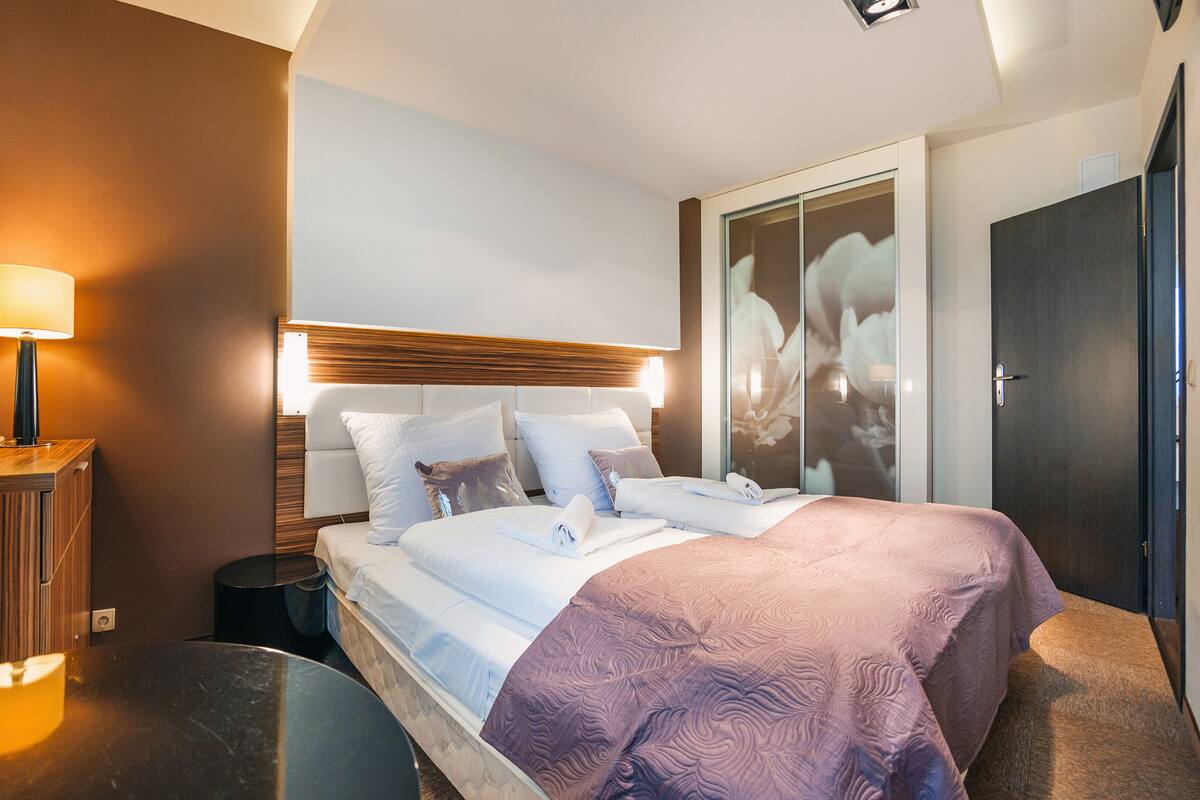 Una habitación de hotel moderna con una cama grande, una mesita de noche, una lámpara y un armario.