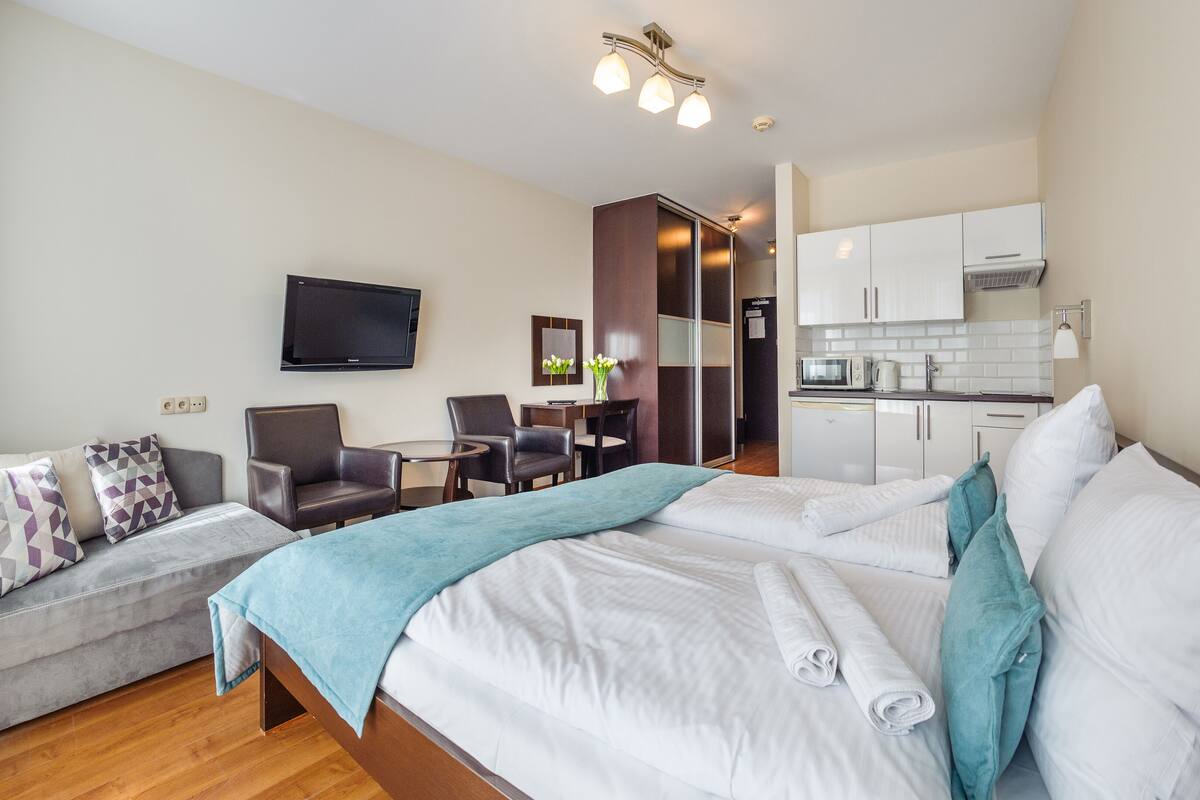 Habitación de hotel con cama, sofá, escritorio, silla, televisor y kitchenette.
