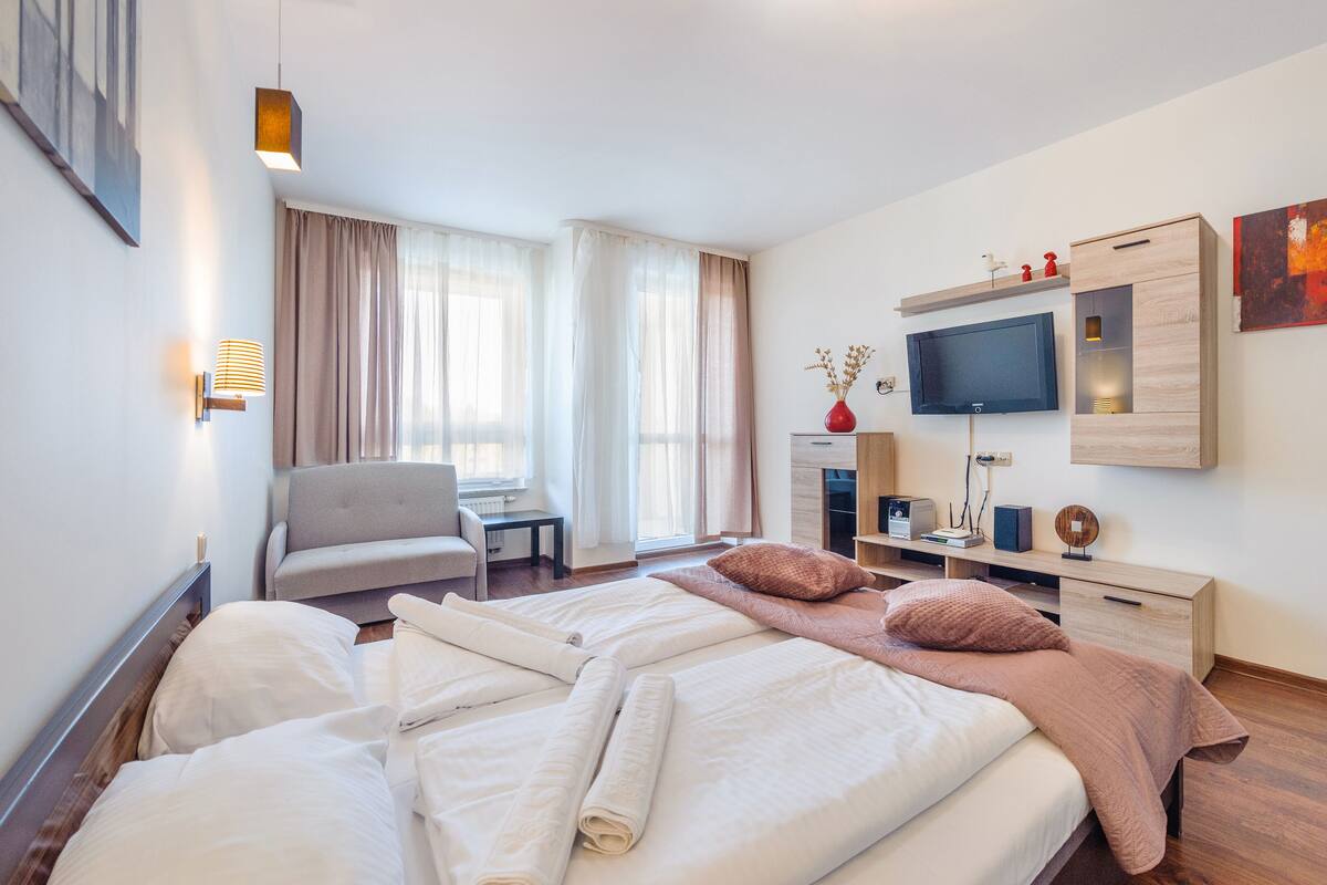 Una habitación de hotel con cama, una silla, un escritorio, televisión y obras de arte en las paredes.