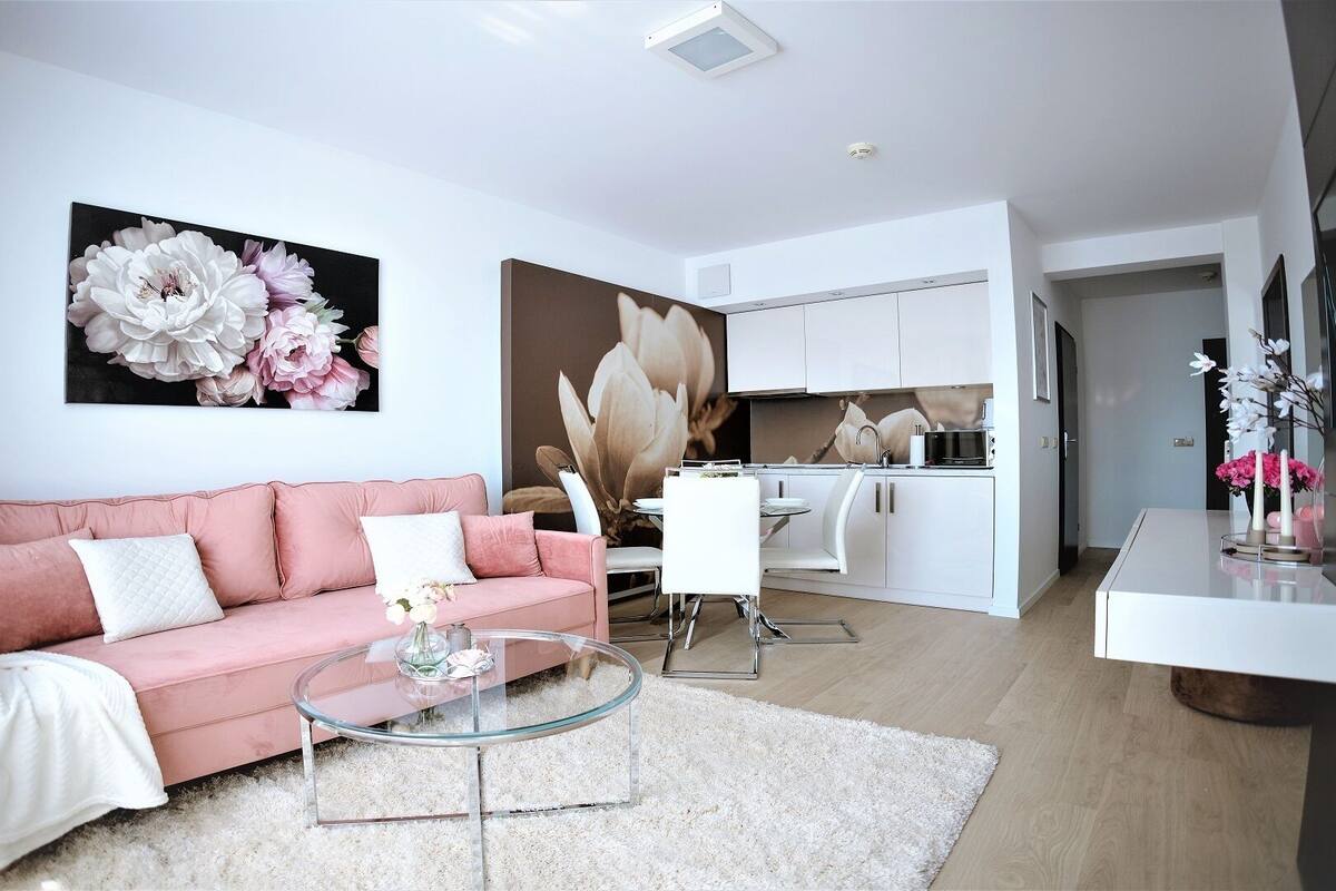 Una sala de estar moderna con un sofá rosa, una mesa de centro de vidrio y una obra de arte floral grande en la pared.
