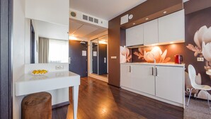 Une cuisine moderne avec des meubles blancs, une table à manger avec des chaises et un petit coin salon avec un tabouret.