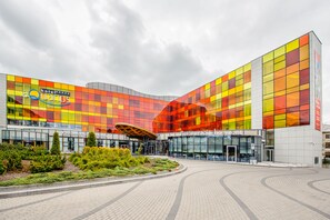 A modern hotel with a colorful facade, a central atrium, and a landscaped entrance area. - Apartamenty Sun & Snow Aquarius Spa (Kolobrzeg)