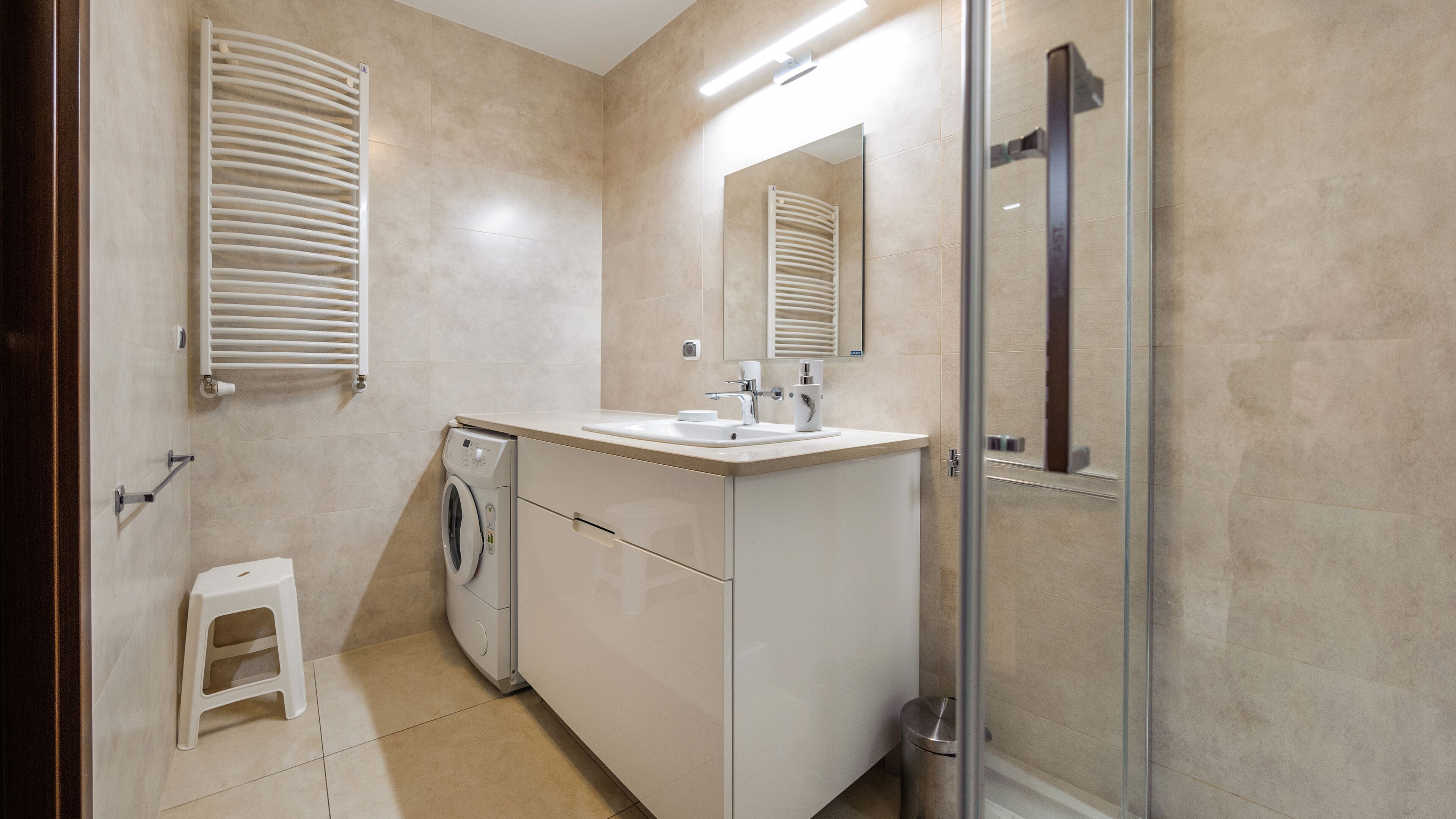 Un bagno moderno con lavatrice, lavabo e cabina doccia in vetro.