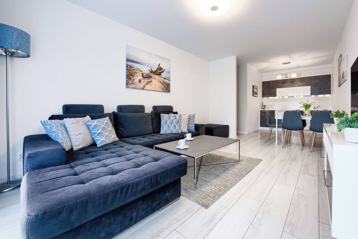 Un salon moderne avec un canapé d’angle bleu foncé, une table basse et un coin repas comprenant deux chaises et une table.