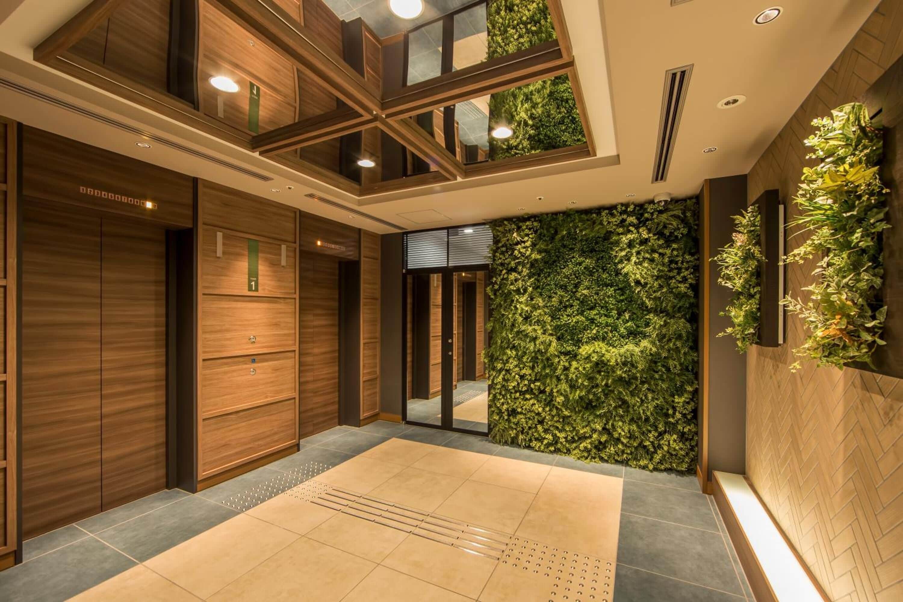 A modern hotel lobby with wooden paneling, a green vertical garden, and a spacious tiled floor.