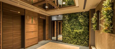 Un moderno vestíbulo de hotel con paneles de madera, un jardín vertical verde y un amplio suelo de baldosas.