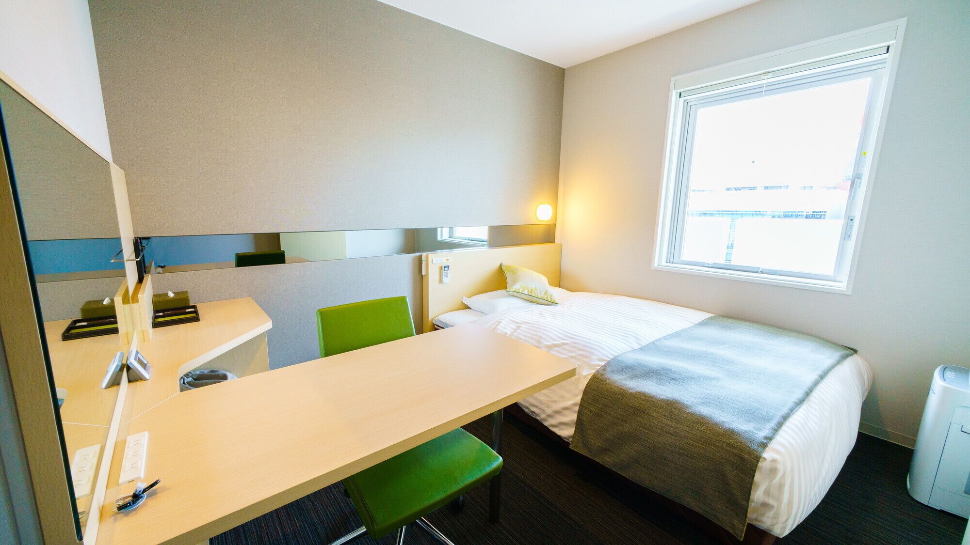 Ett hotellrum med en säng, ett skrivbord, en stol, ett fönster och en spegel.