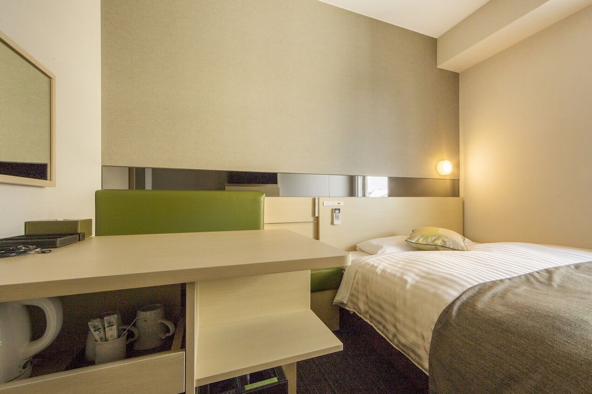 Una habitación de hotel con cama, escritorio, teléfono, espejo y ventana.