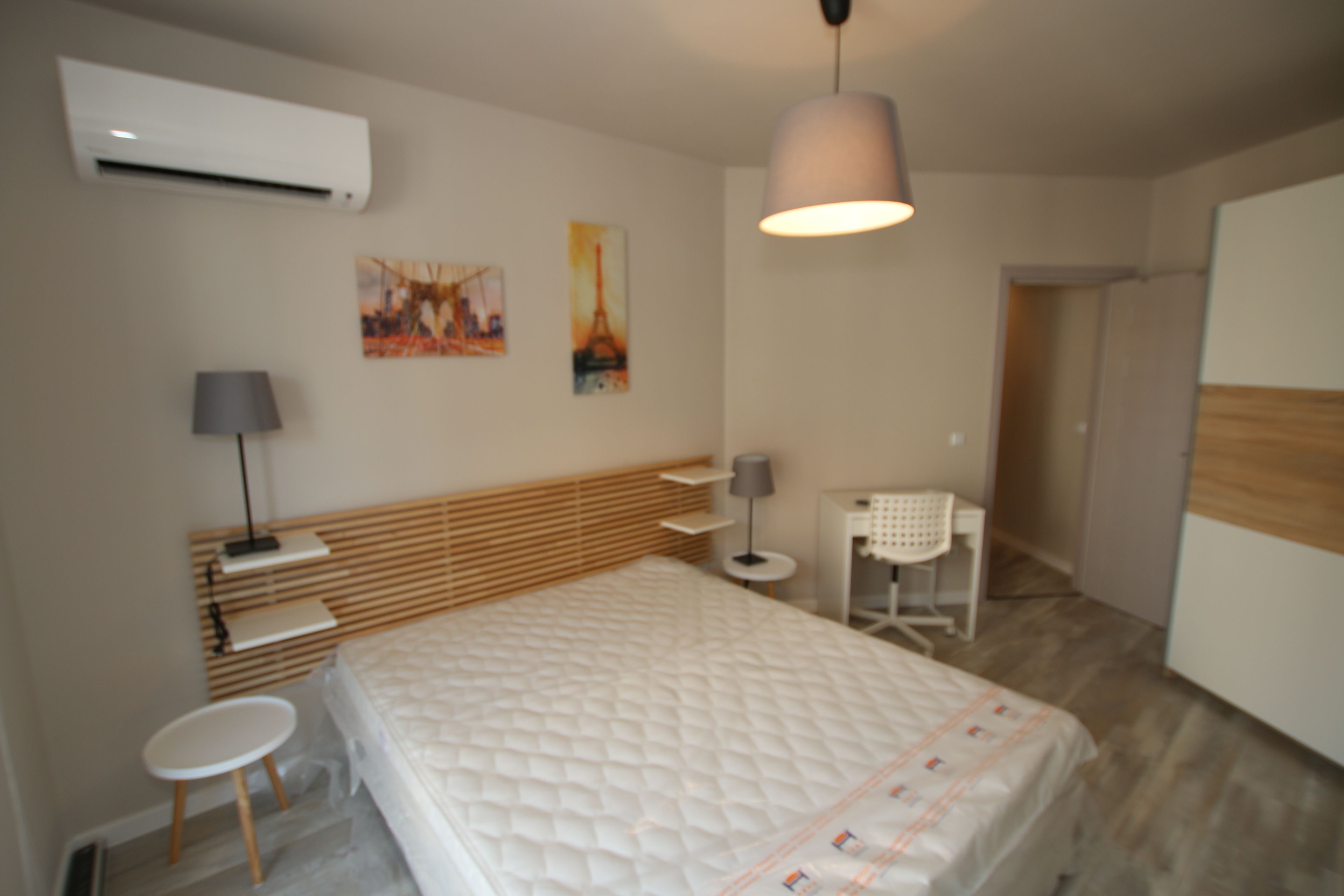 A modern hotel room with a large bed, a desk, a chair, and a small table.