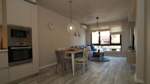 A modern kitchen with built-in appliances, a dining area with a table and chairs, and a view of the outside through large windows. - Apartments Angelov (Varna)
