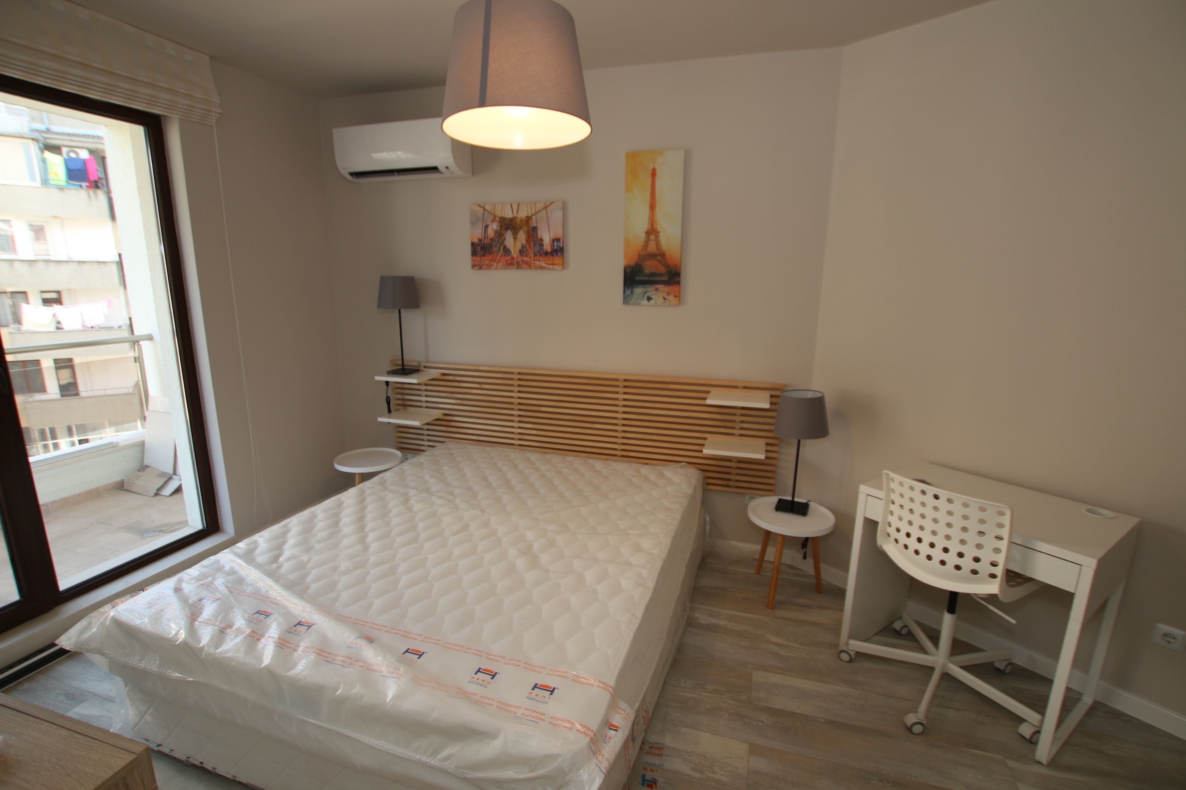 A bedroom with a bed, a desk, a chair, and artwork on the wall.