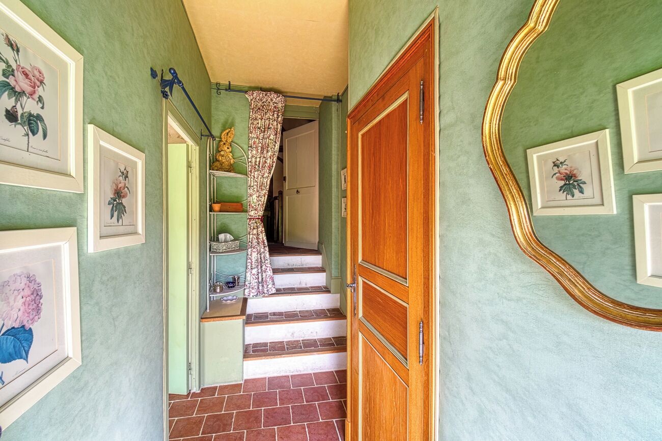 A hallway with green walls, framed floral artwork, a wooden door, and a staircase with red tiles.