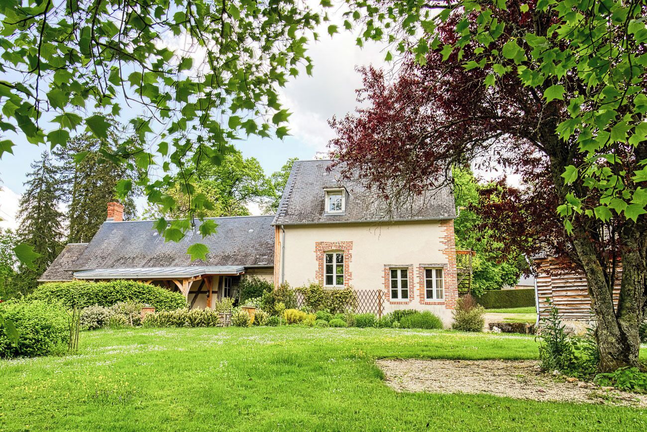 Een huis met een schuin dak, een bakstenen schoorsteen en een verzorgde tuin met gazon en diverse planten.