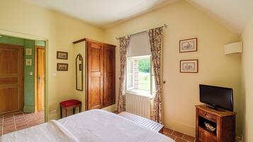 A bedroom with a bed, wooden wardrobe, a small table with a television, and a window with curtains.