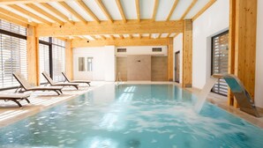 Una piscina interior con vigas de madera, sillones de descanso y una fuente de agua.