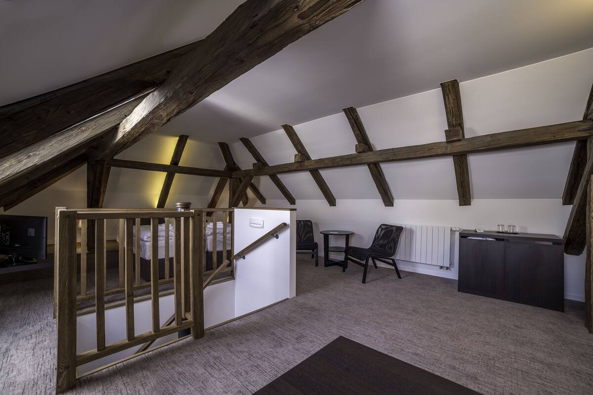 A loft-style room with exposed wooden beams, a staircase, a small table, a chair, and a cabinet.