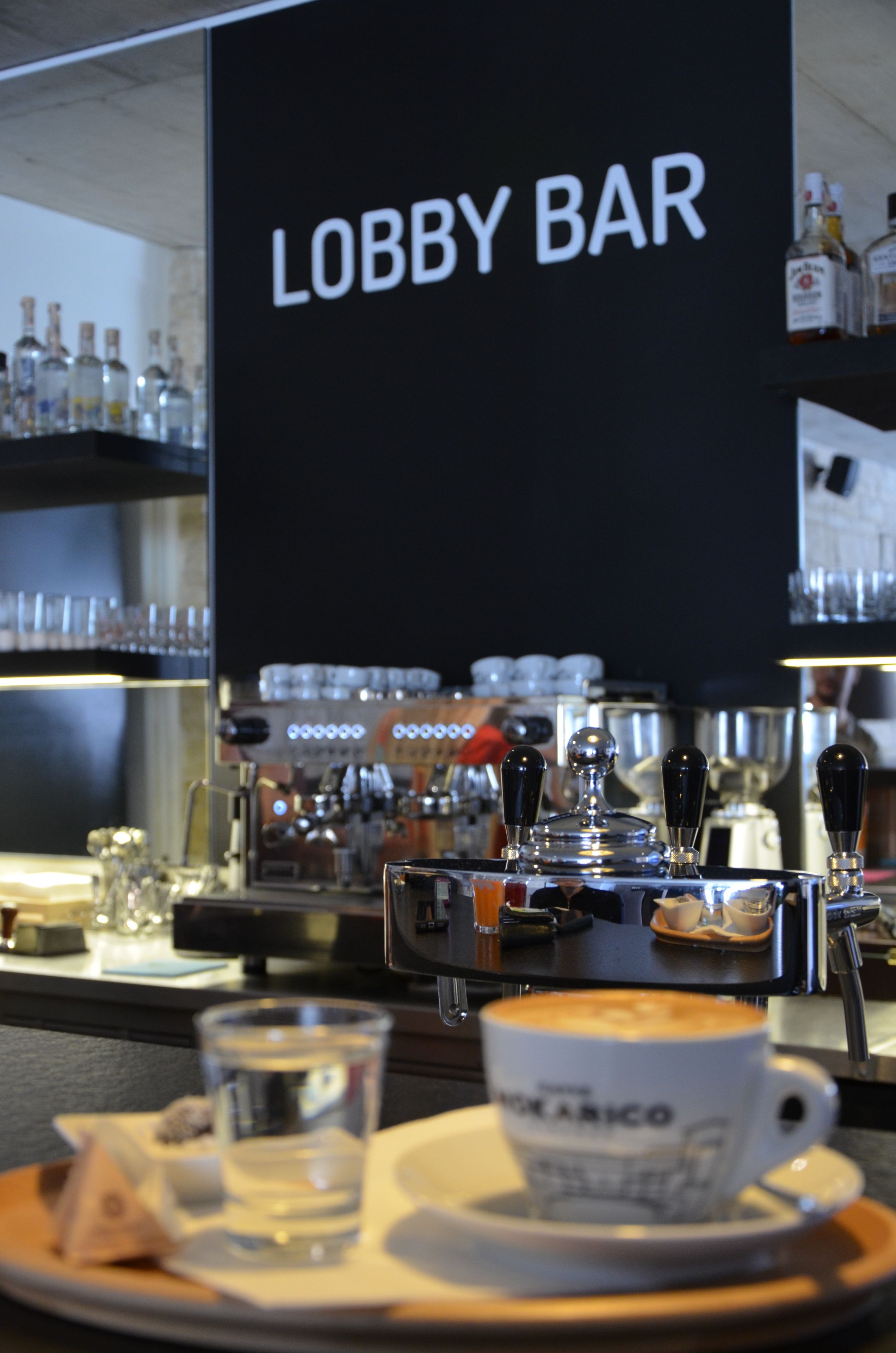 A bar area with a sign reading "Lobby Bar," espresso machines, and a cup of coffee on a tray.