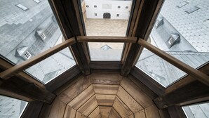 Vista aérea de una habitación con suelo de madera y ventanas amplias, con vistas a un patio con edificios.