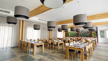 Un vaste espace dédié à la salle à manger, avec de nombreuses tables et chaises, de grandes suspensions décoratives et une vue sur un mur végétal agrémenté de fleurs.