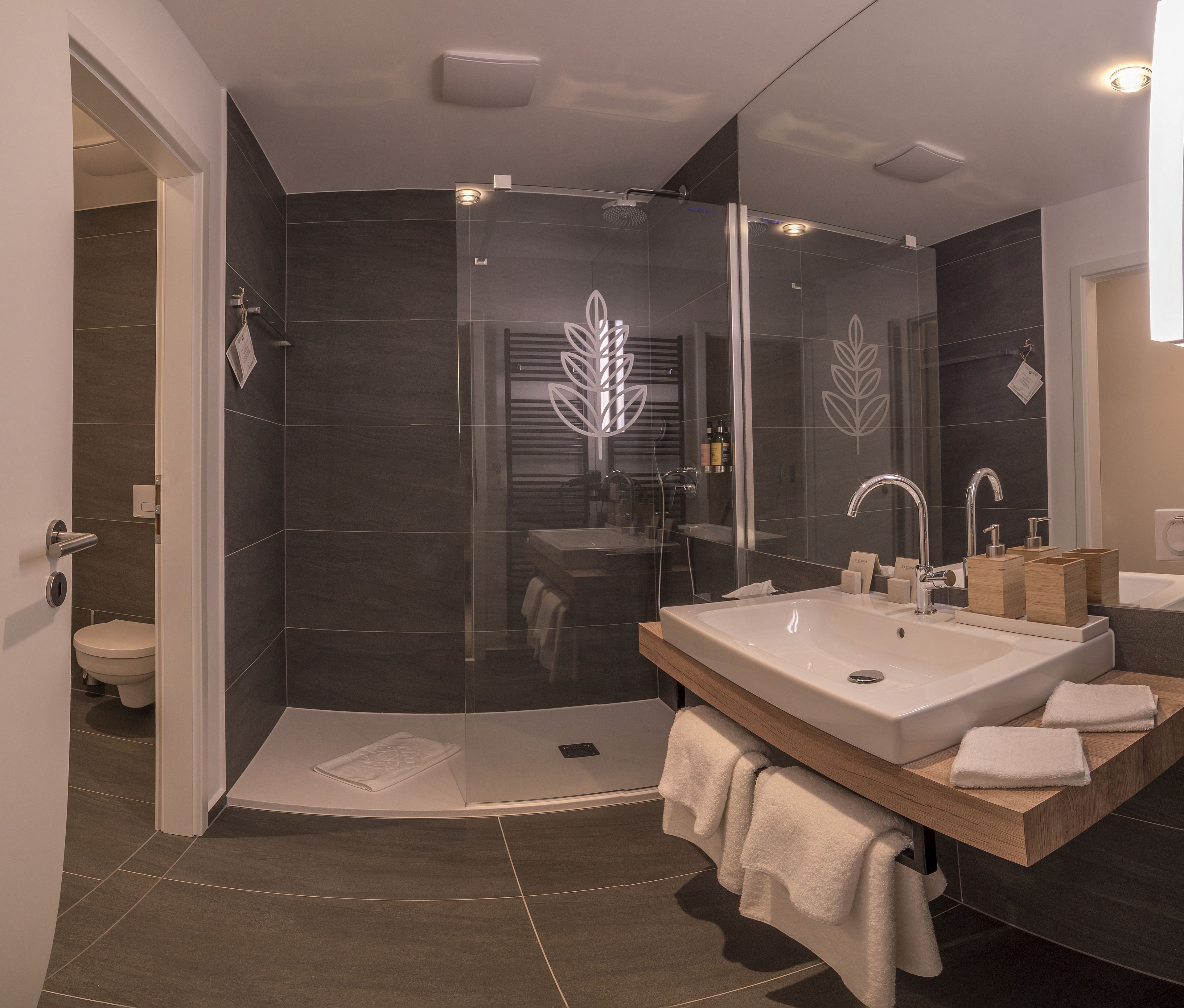 Un baño moderno con ducha envuelta en vidrio, un lavamanos grande y un mueble de tocador de madera.