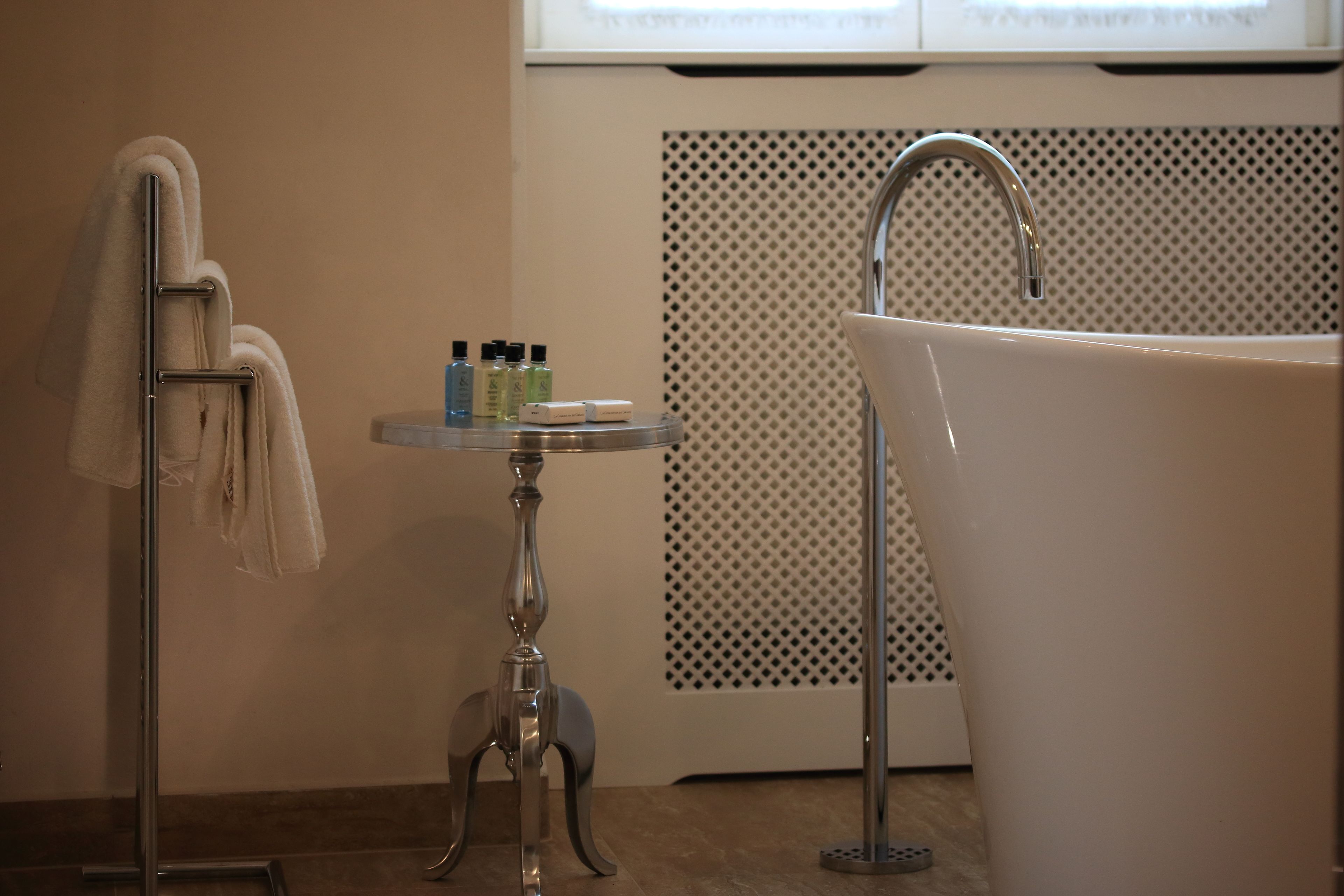 Un baño con bañera, un perchero para toallas y una mesita con artículos de aseo.