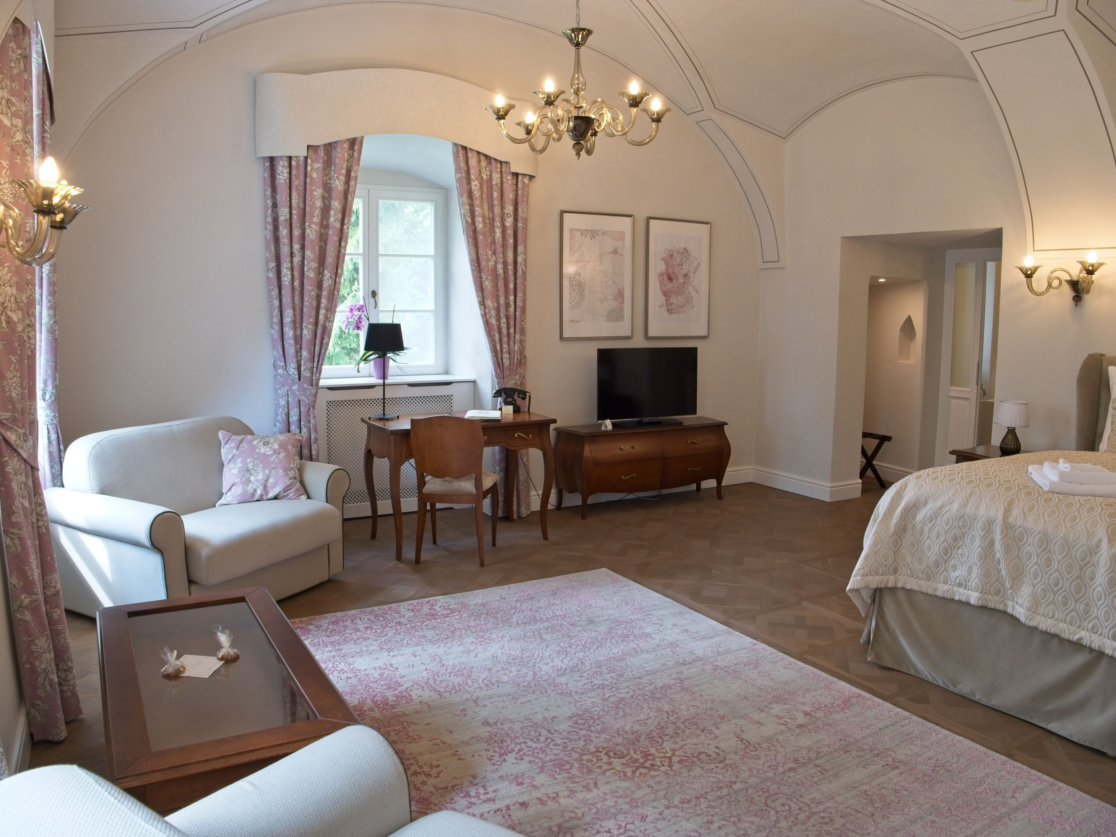 Habitación de hotel con cama, escritorio, sillón, sofá, televisor y candelabro.