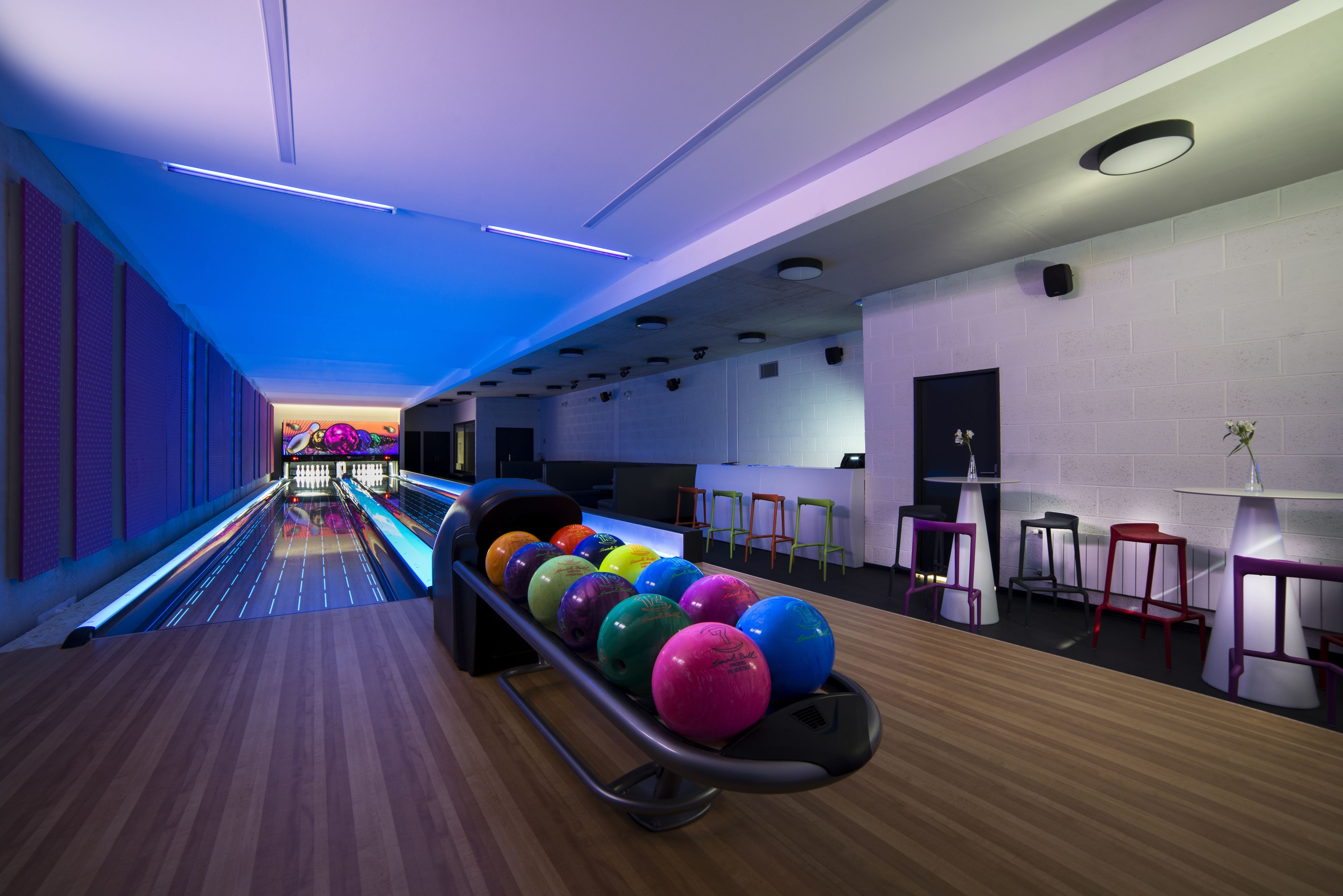 A bowling alley with lanes, a ball return rack, and bar stools.