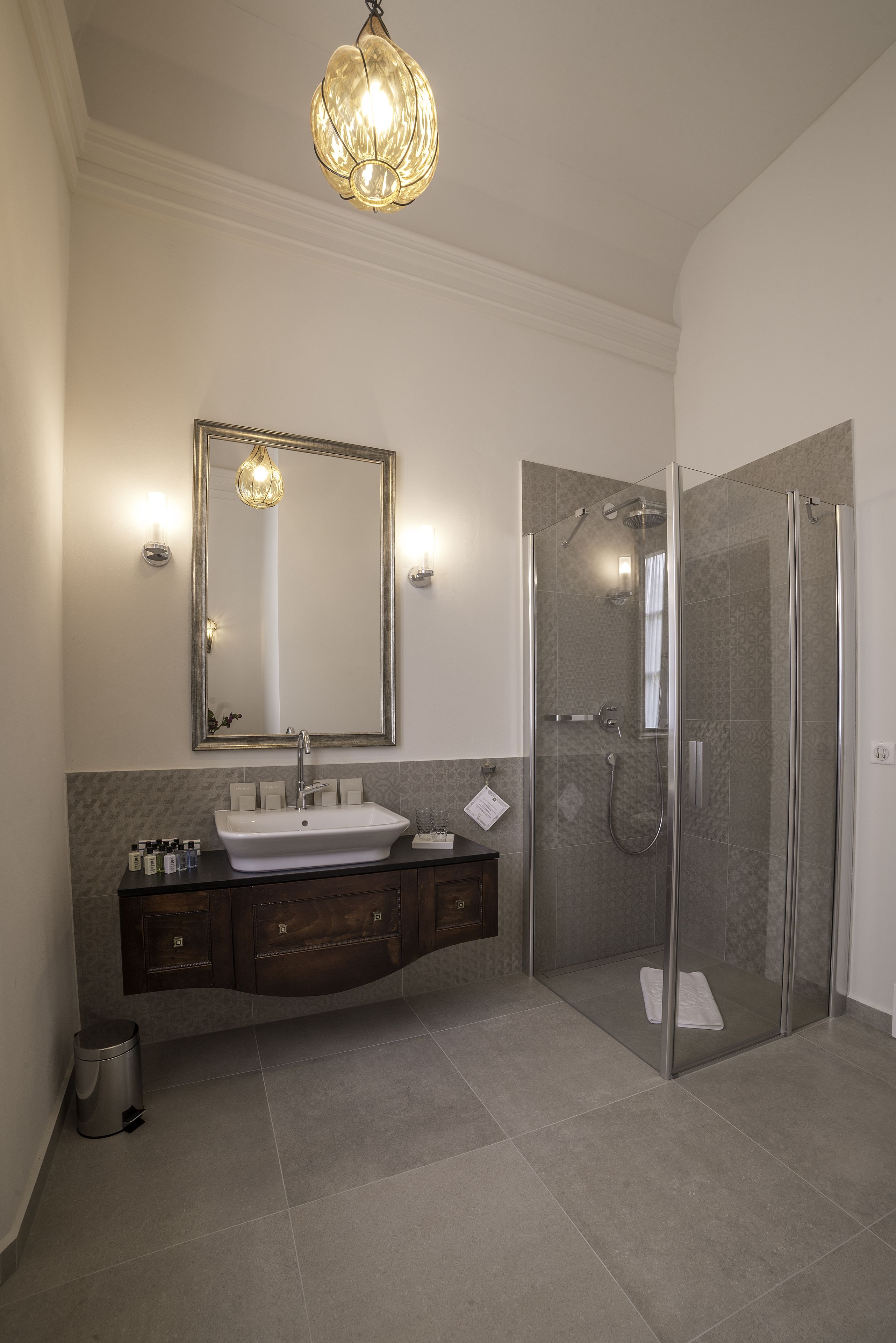 A modern bathroom with a large mirror, a sink, a shower enclosure, and a hanging light fixture.