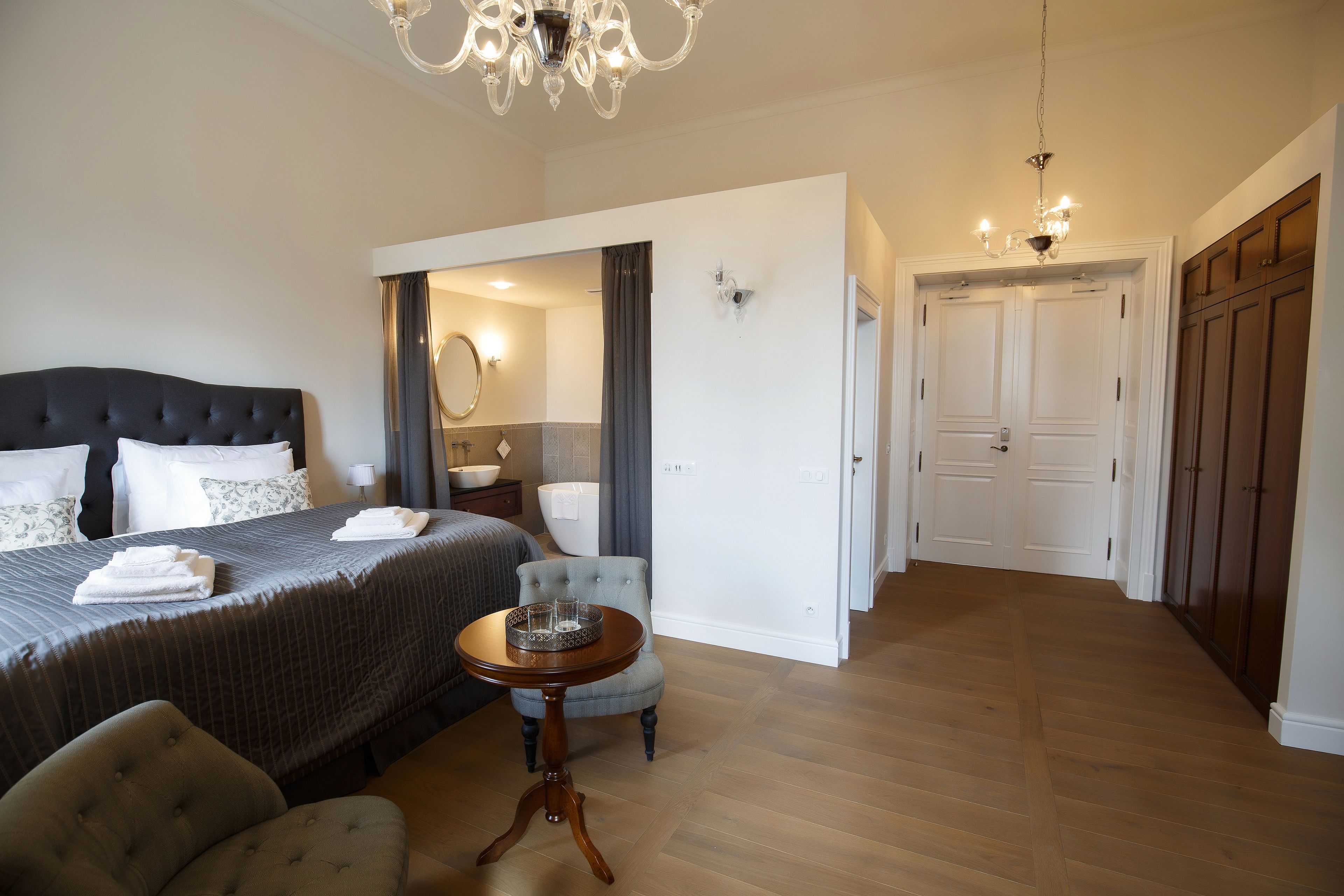 A hotel room with a large bed, a round table, a chair, and a chandelier.