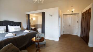 A hotel room with a large bed, a round table, a chair, and a chandelier.