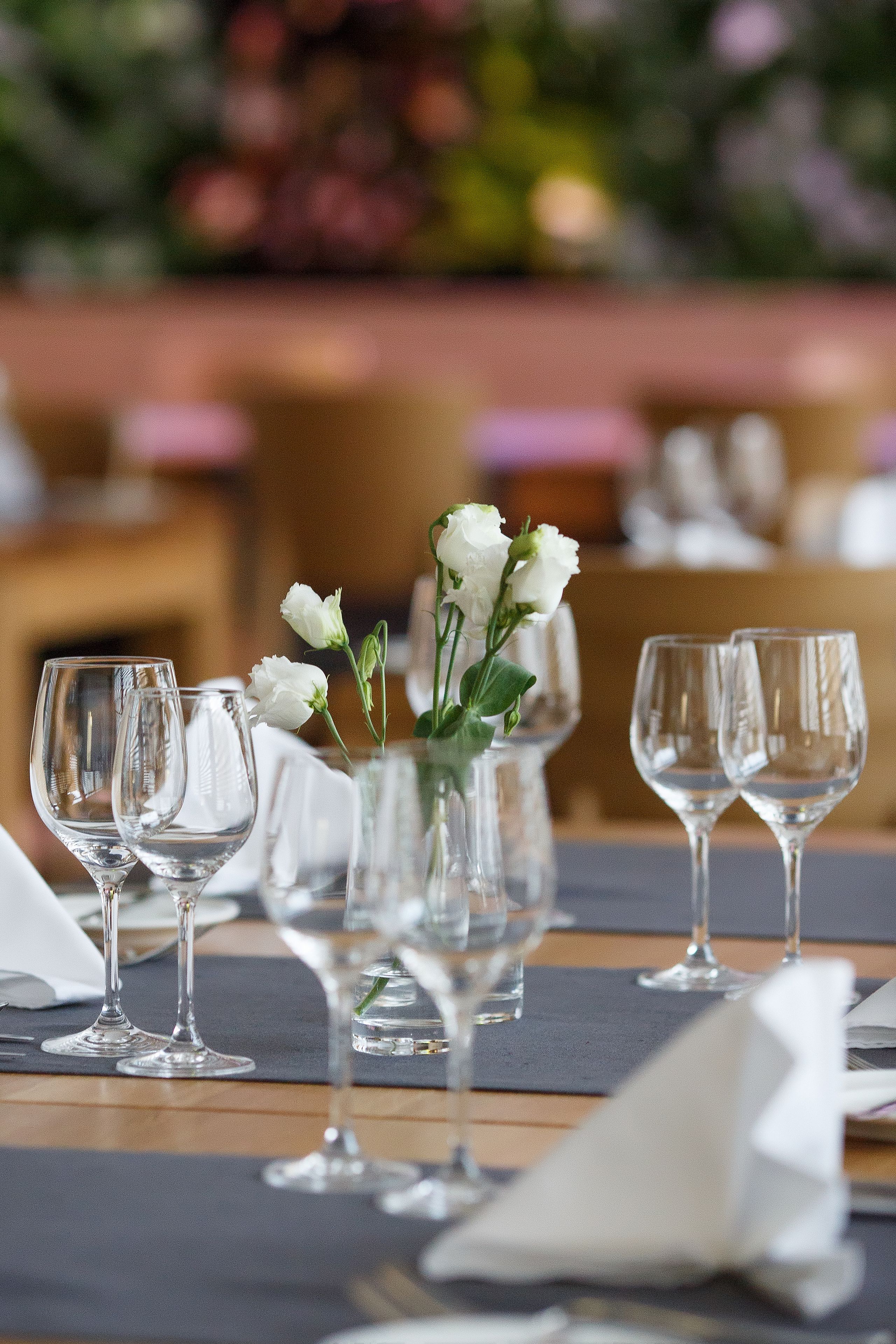 Una mesa de comedor dispuesta con copas de vino y un florero con flores blancas.