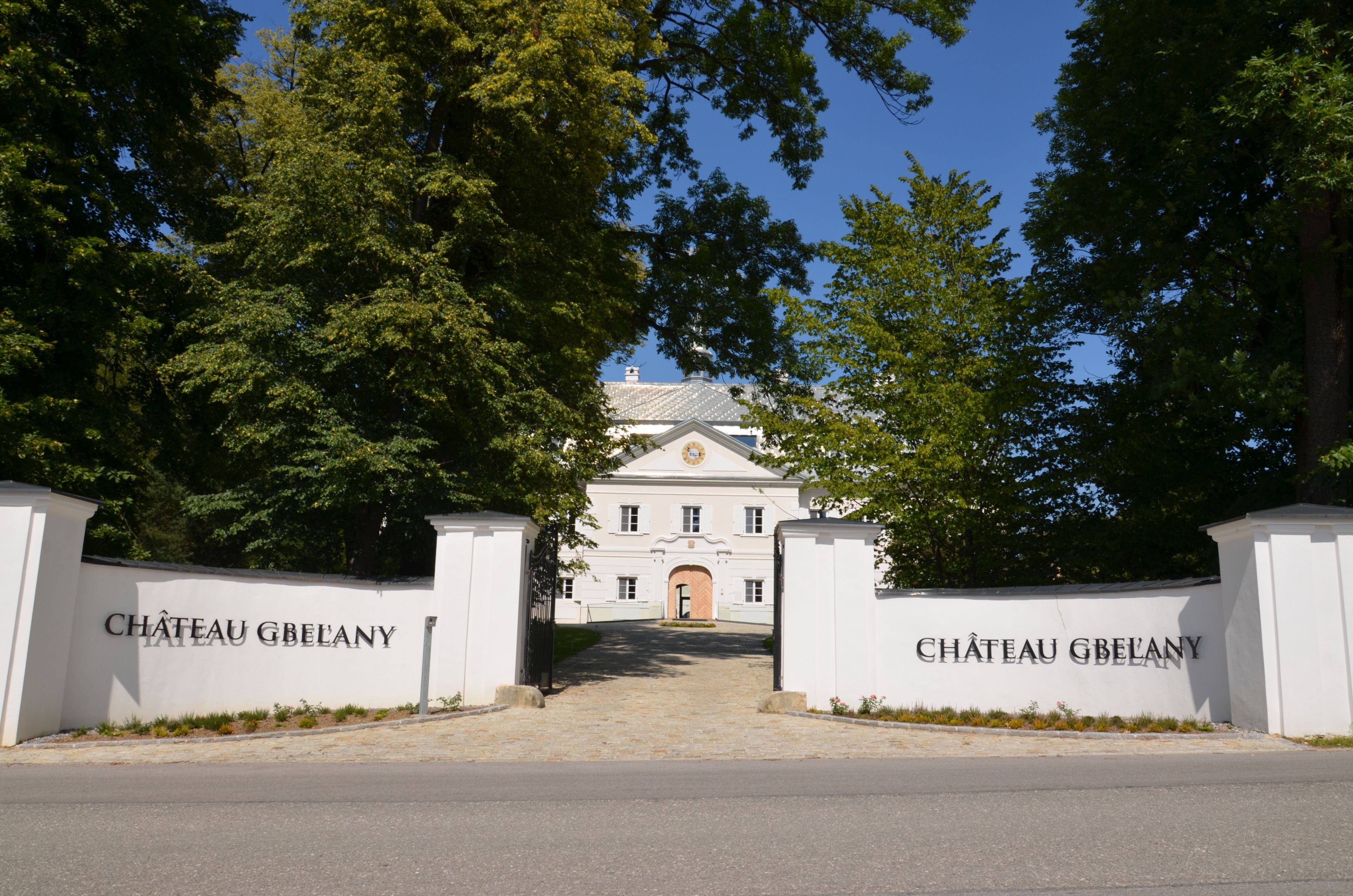 Ein imposanter Eingangsbereich mit einer weißen Mauer und einem Tor, auf dem "CHÂTEAU GBEANY" steht.