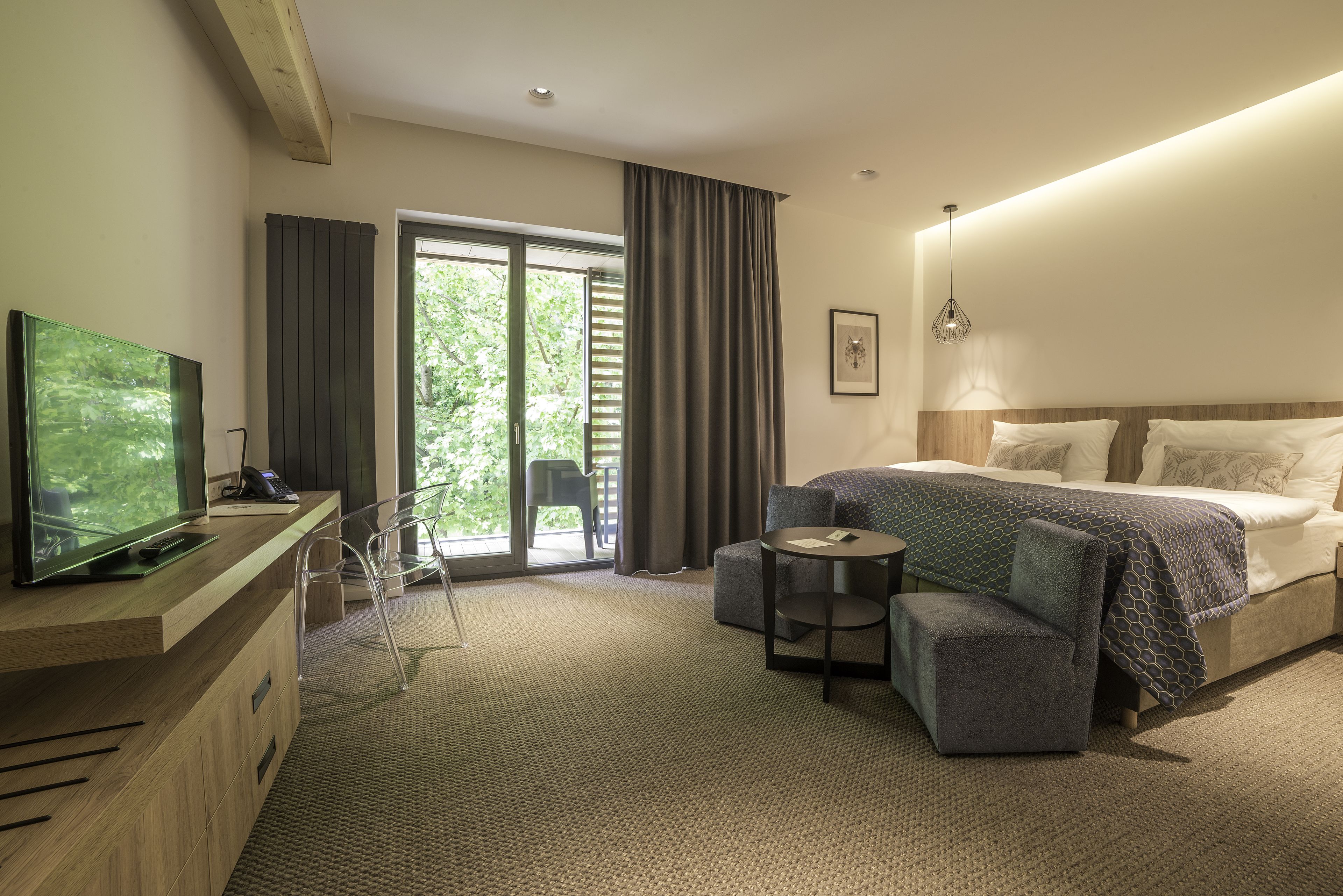 Habitación de hotel moderna con una cama grande, un escritorio con televisor de pantalla plana, una mesita y vista a zonas verdes a través de una puerta corrediza de cristal.
