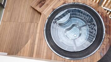 Un jacuzzi circular en una terraza de madera con un banco de madera y una barandilla de metal.