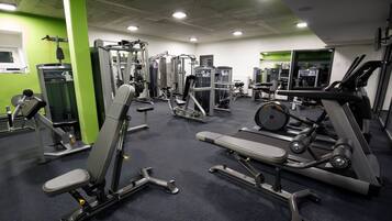 Une salle de sport équipée de divers appareils d’exercice, d’un banc de développé et d’un tapis de course.