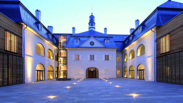 Un patio amplio con una edificación central que presenta arcos y una imponente torre del reloj.
