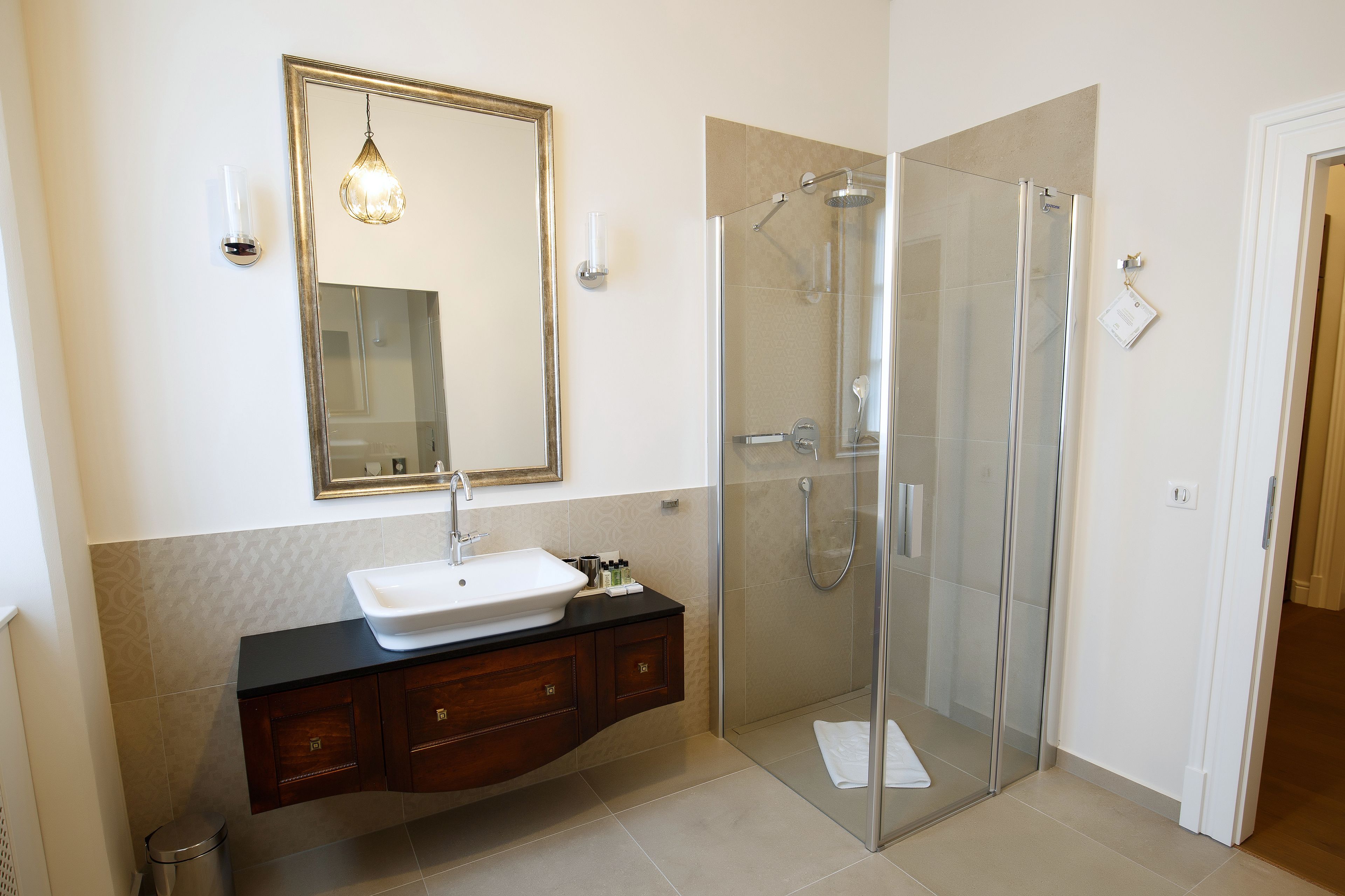 Un baño moderno con ducha separada por vidrio, lavamanos blanco y un espejo grande.