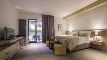 A hotel room with a bed, bedside table, lamp, TV, desk, chair, and a view of the outdoors.