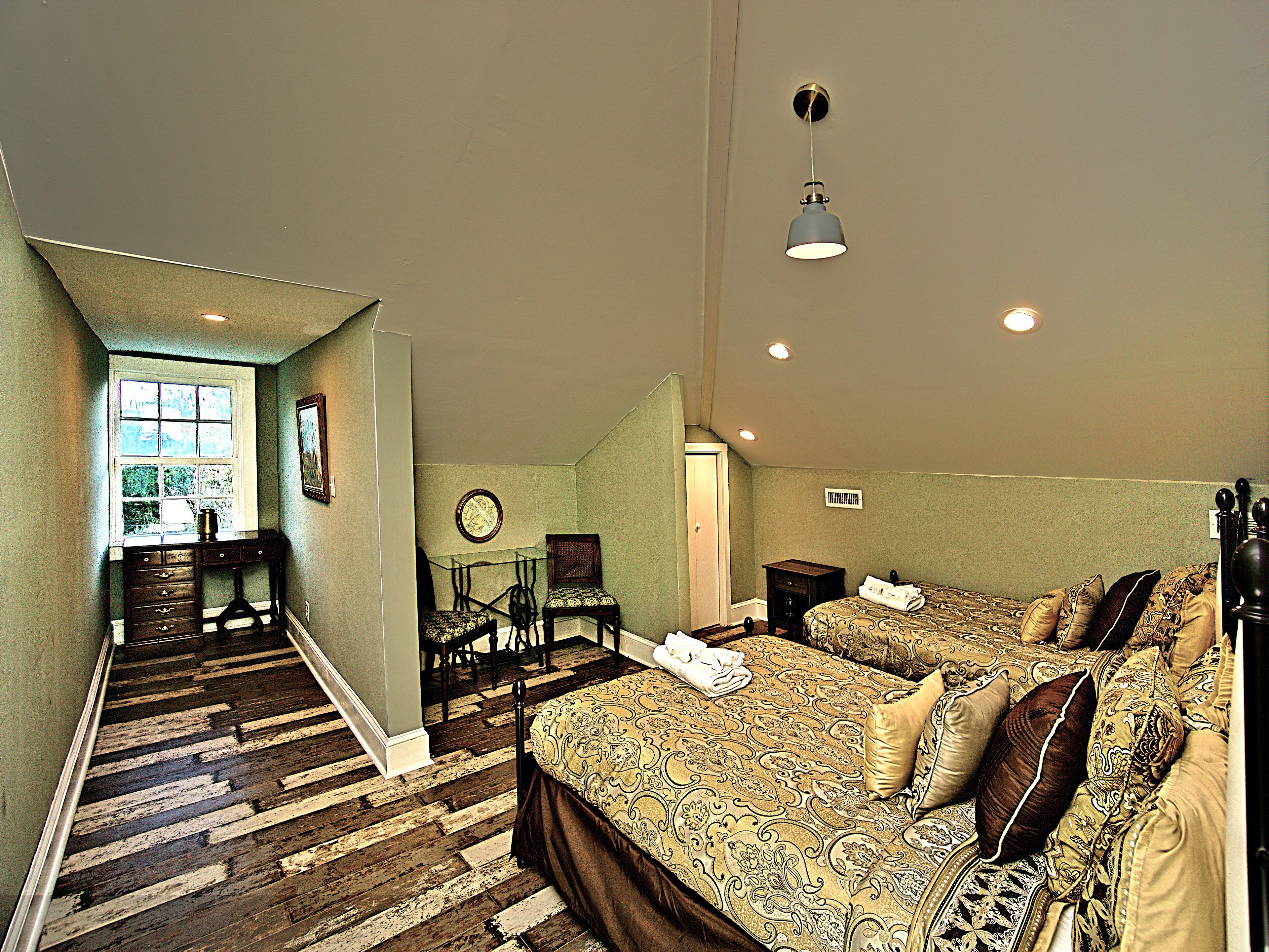 A bedroom with a large bed, a desk, and a chair. There is a window and a door leading to another room.