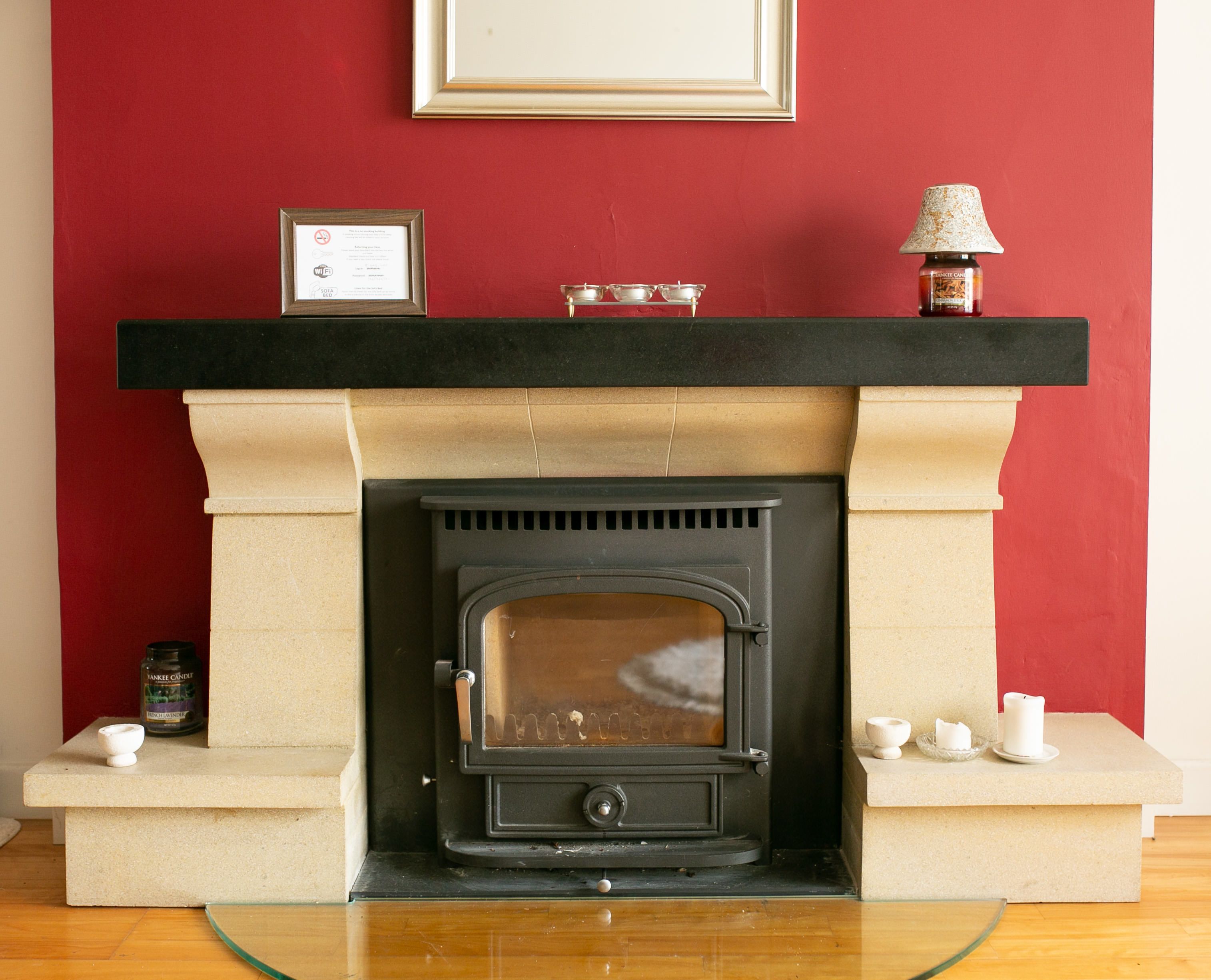 A fireplace with a black mantel, a framed certificate above it, and a candle holder to the right.