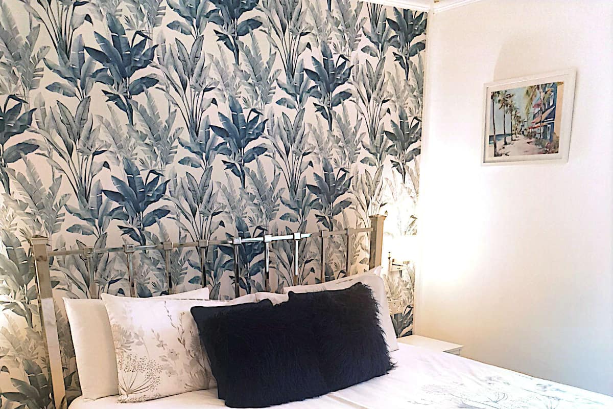 Una cama bien hecha con una colcha floral, un almohadón negro y un cabecero de metal.