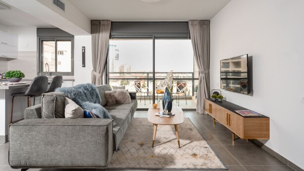 A modern living room with a grey sofa, a coffee table, and a TV mounted on the wall.
