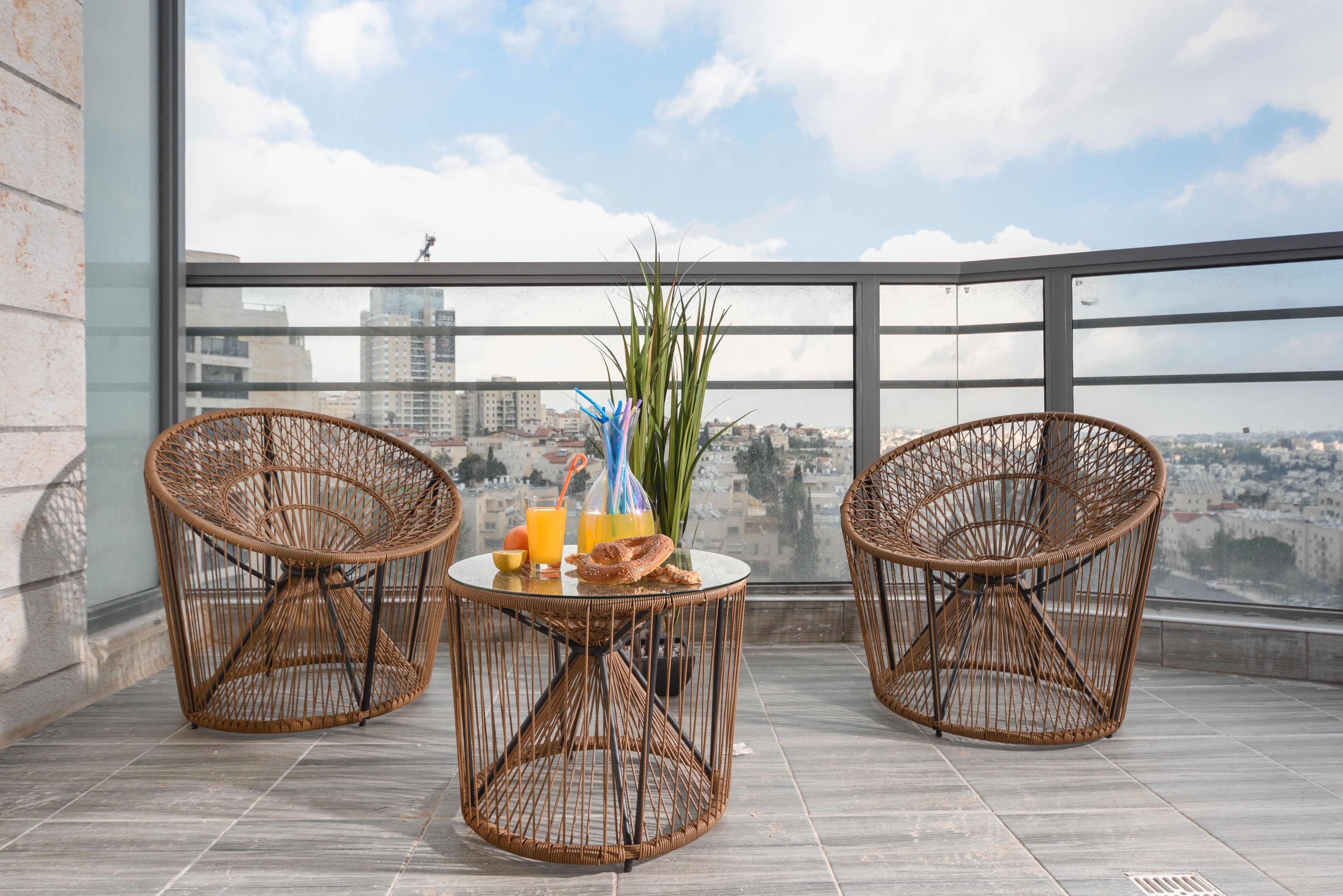 A balcony with wicker chairs, a small table, and a view of the cityscape.