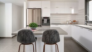 A modern kitchen with white cabinets, stainless steel appliances, and two grey chairs.