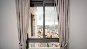 A window with curtains, offering a view of a cityscape with buildings and roads.