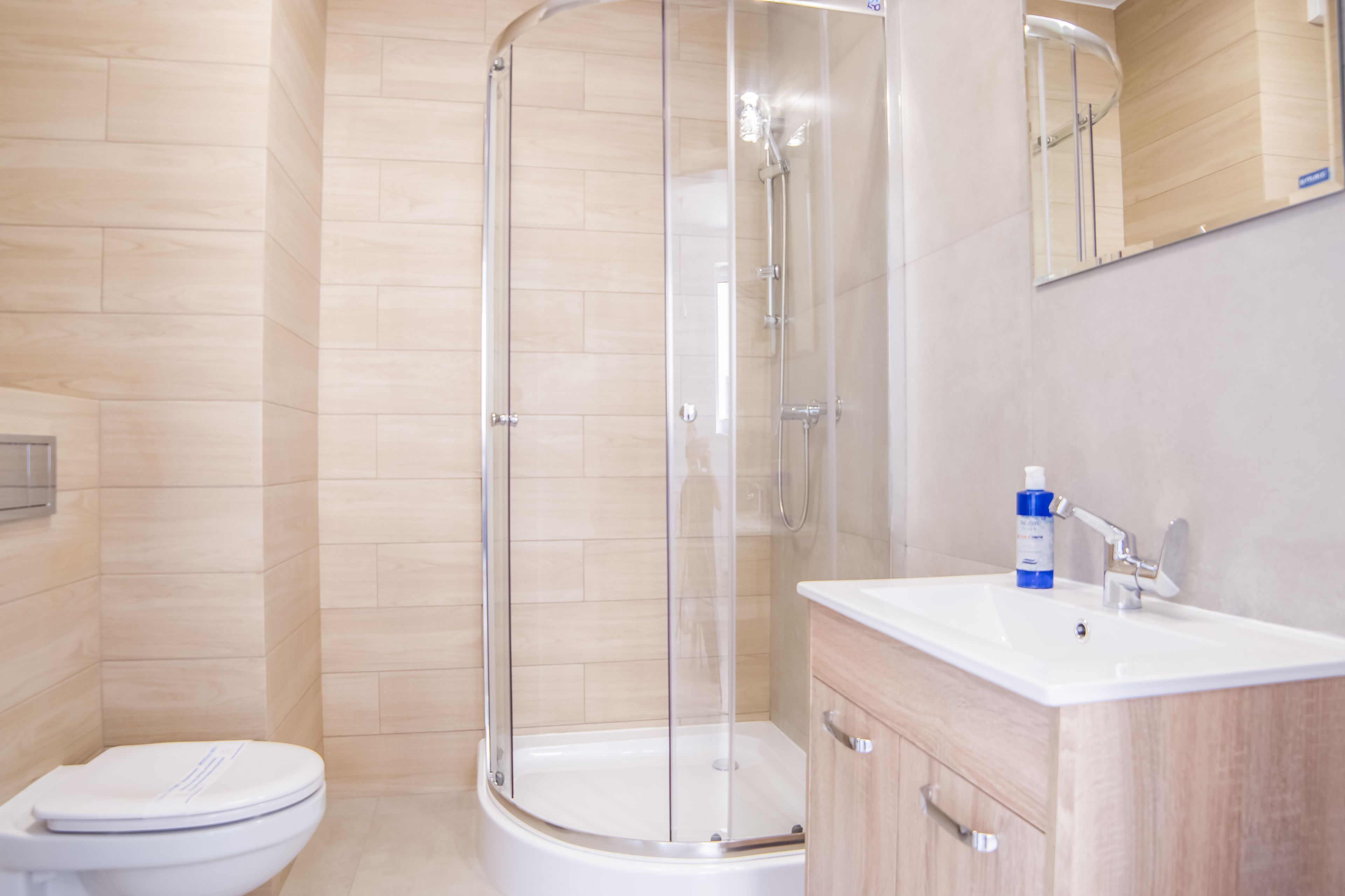 A modern bathroom with a glass-enclosed shower, a white toilet, and a wooden vanity with a sink.