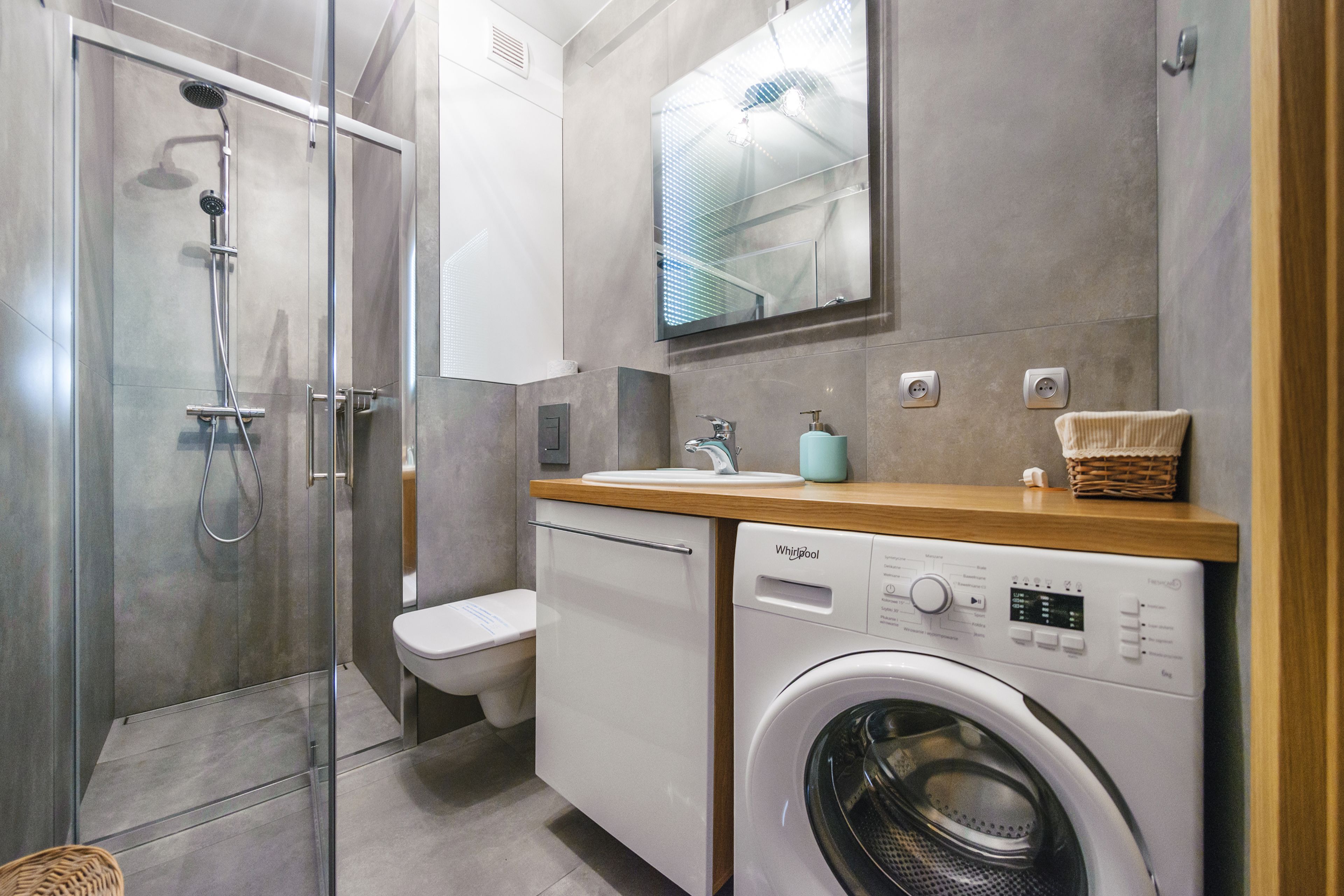 Ett modernt badrum med en duschavdelning med glasväggar, en toalett och en tvättmaskin av märket Whirlpool med frontmatning.