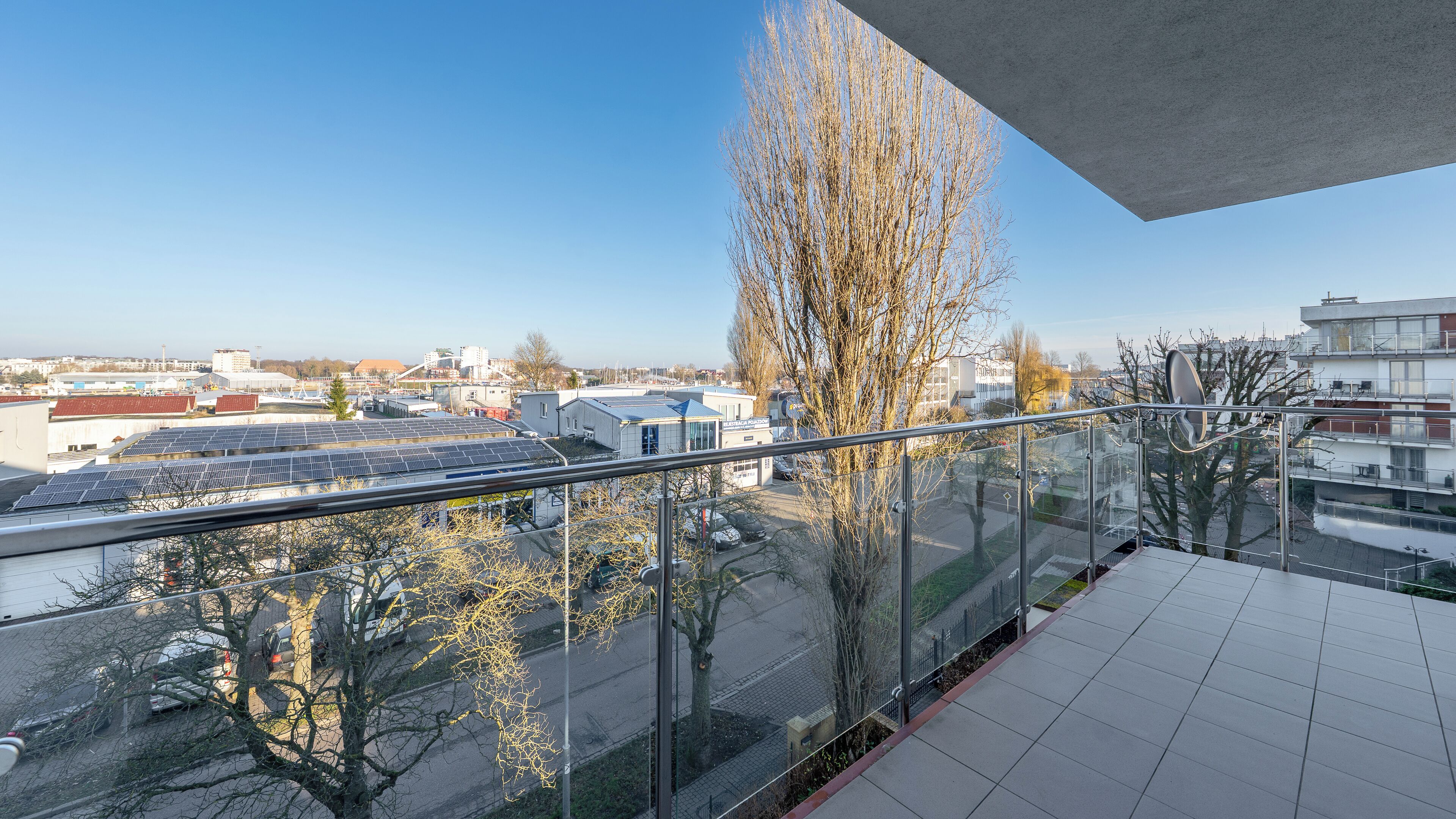 Een balkon met een helder uitzicht op zonnepanelen, een boom en gebouwen op de achtergrond.