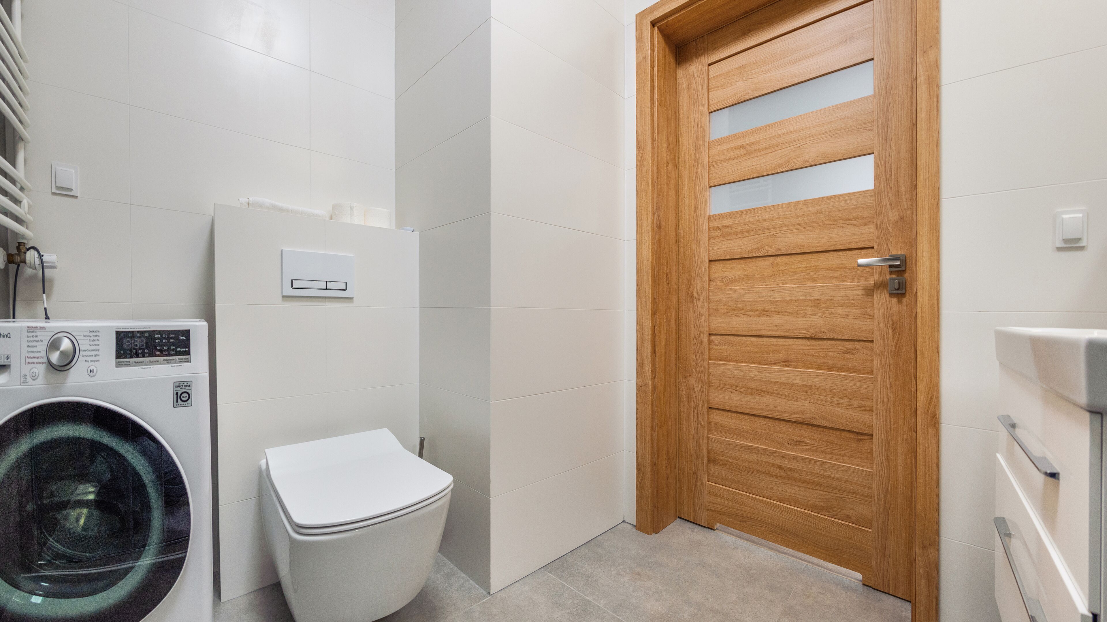 A compact bathroom with a washing machine, a toilet, and a wooden door.
