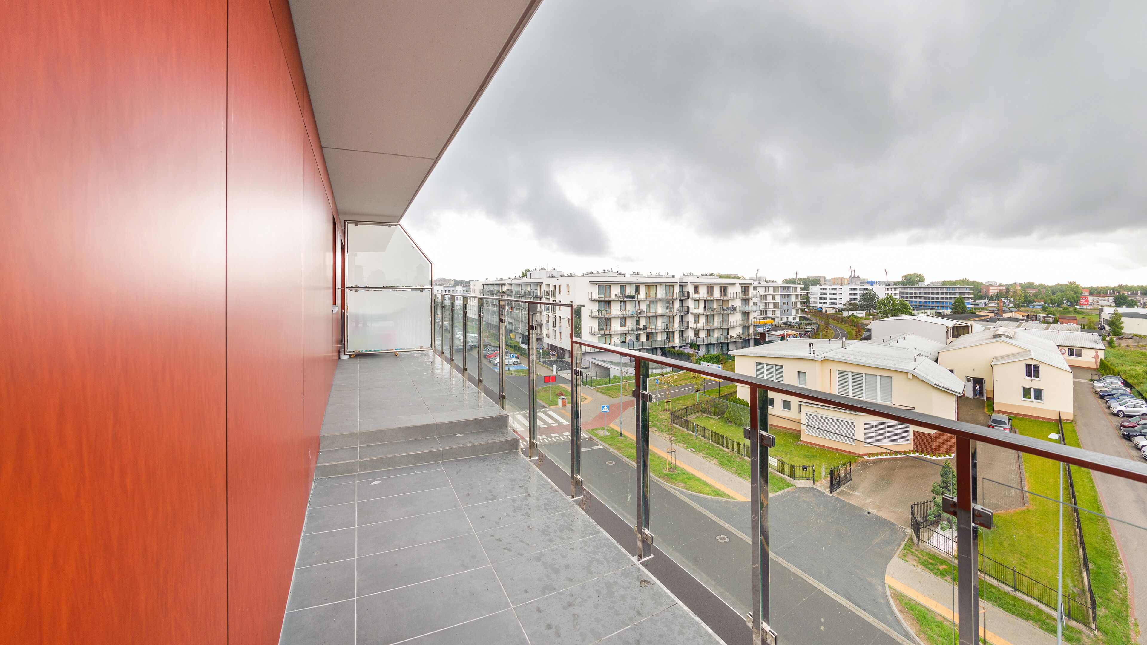 A balcony with a view of a residential area, including multi-story buildings and parked cars.